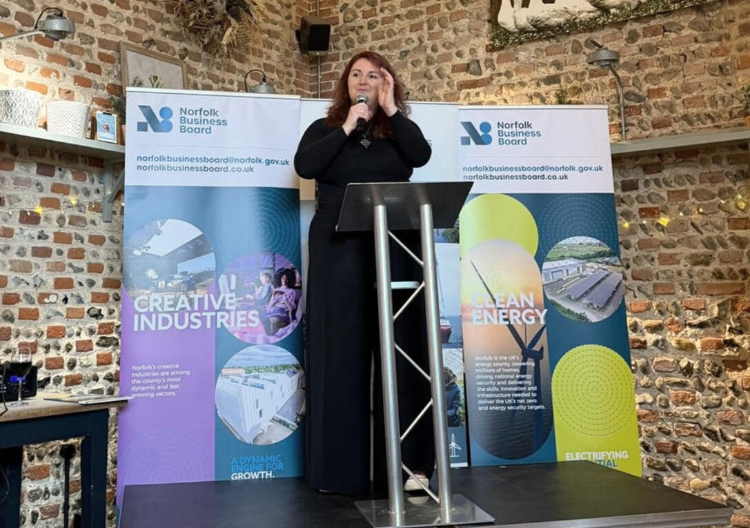 Robin Milton stands behind a podium, speaking at a Norfolk Ambassadors Event.